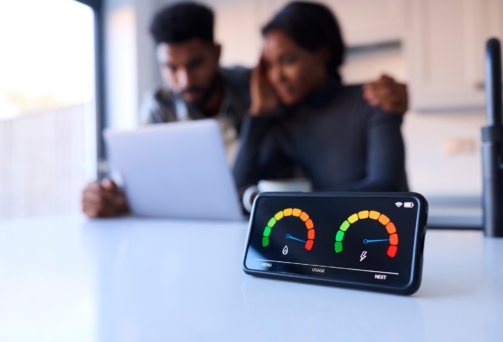 Worried Couple At Home Looking At Laptop With Smart Energy Meter In Foreground